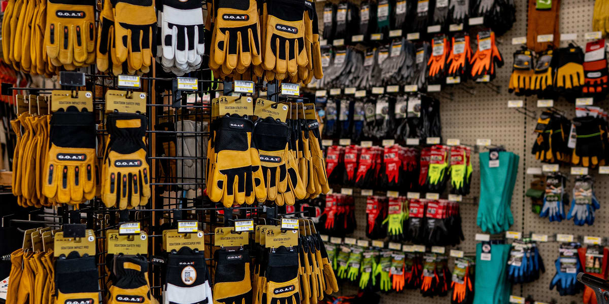 A hardware store aisle displaying an extensive selection of work gloves, with prominent G
