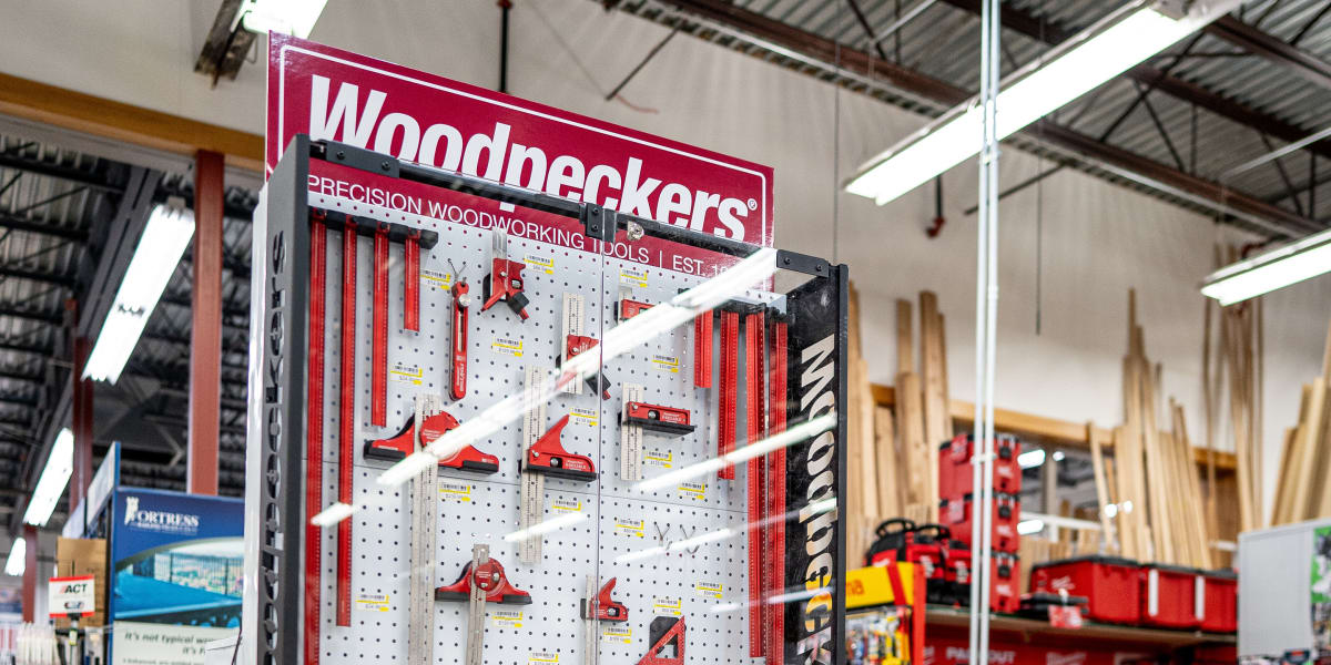 A Woodpeckers precision woodworking tools display rack in a hardware store, featuring red-handled measuring tools, squares, r