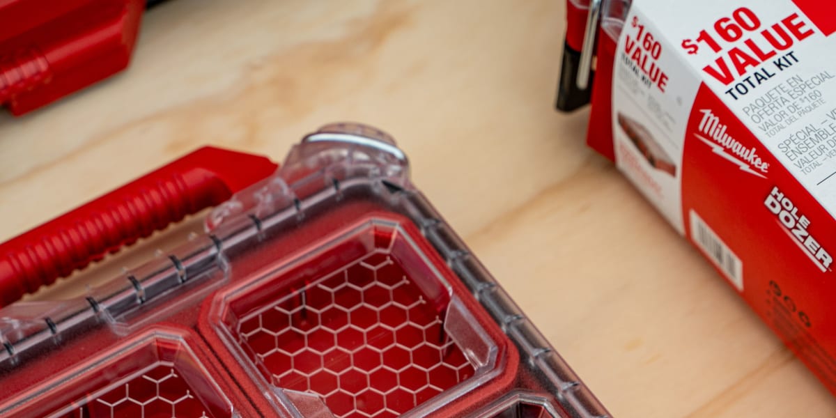 A clear plastic Milwaukee Packout modular storage case is open, displaying multiple compartments with hexagonal mesh dividers