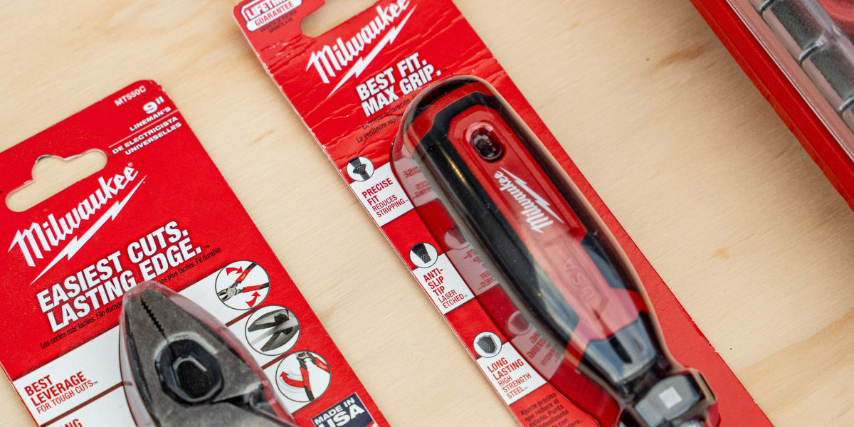 Close-up product photo showing two Milwaukee tools in their original red retail packaging on a wooden surface