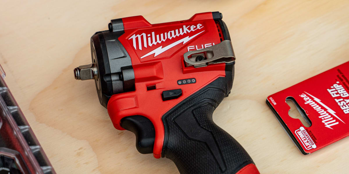 A Milwaukee FUEL cordless impact wrench sits on a wooden workbench surrounded by red Milwaukee tool storage containers with c