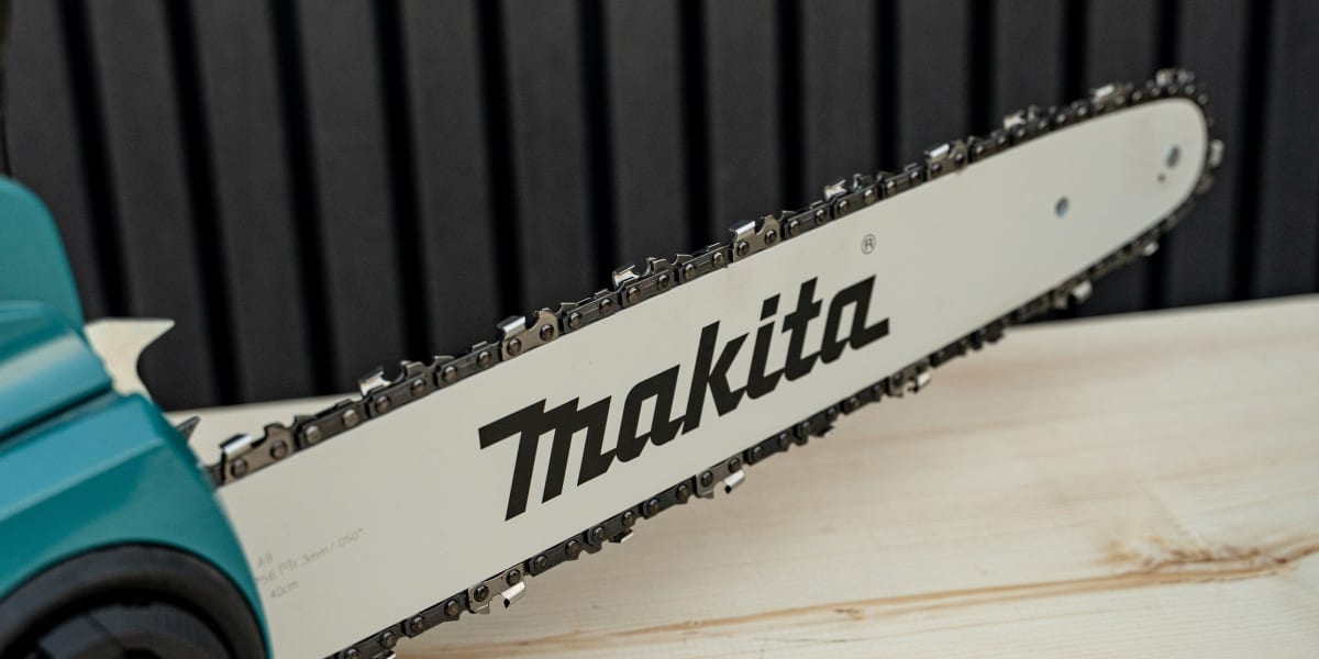 A Makita chainsaw with its white guide bar and chain prominently displayed, sitting on light-colored wooden planks