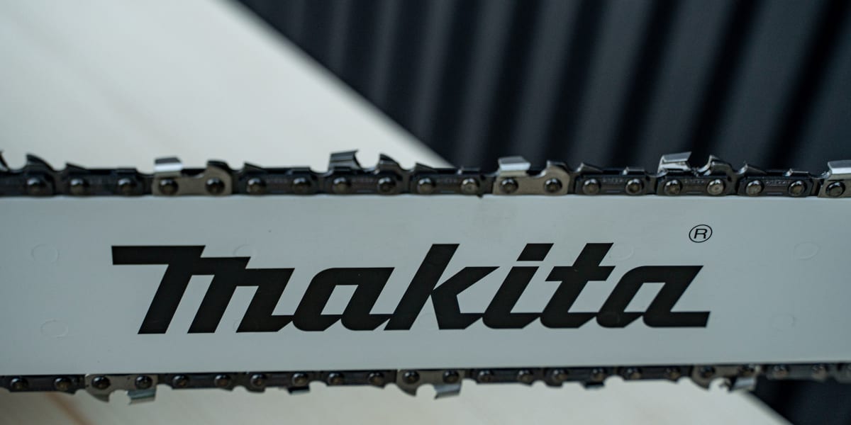 Close-up product detail shot of a Makita chainsaw showing the guide bar with sharp cutting chain teeth