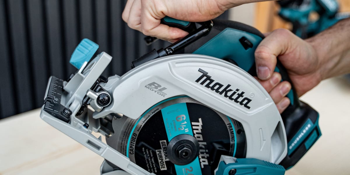 A person's hands operating a Makita cordless circular saw, cutting through a piece of light-colored wood lumber
