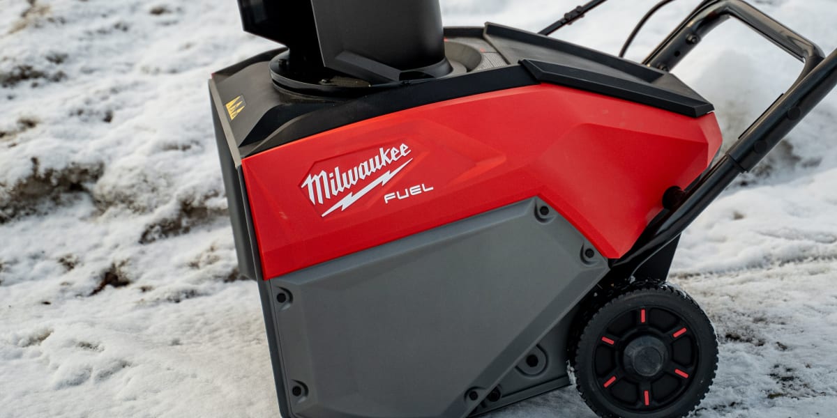 A Milwaukee Fuel cordless snow blower sitting on snowy ground with a large pile of snow in the background