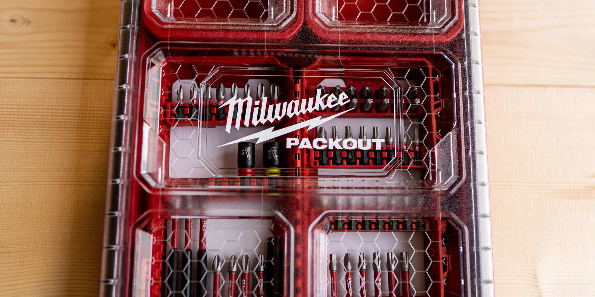A Milwaukee PACKOUT modular storage organizer case with clear lid and red base, featuring multiple compartments with hexagona
