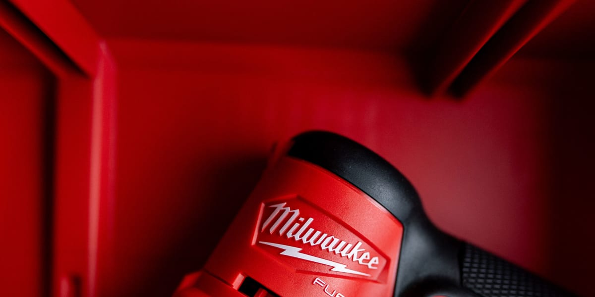 A close-up product shot of a Milwaukee FUEL cordless orbital sander with red and black housing and textured grip handle