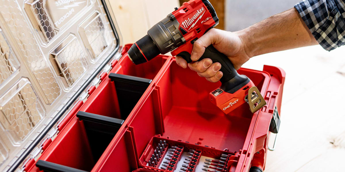 A person's hand holding a red Milwaukee cordless drill while retrieving it from a red Milwaukee PACKOUT tool storage system
