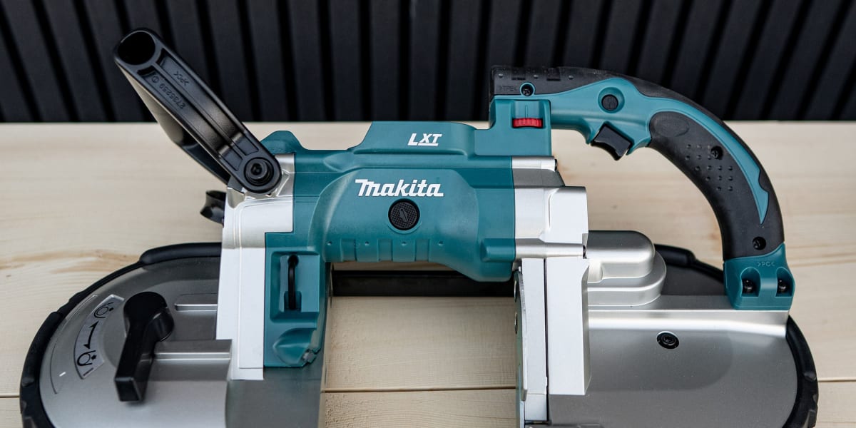 A Makita LXT cordless band saw power tool positioned on a light wooden surface against a dark corrugated metal background