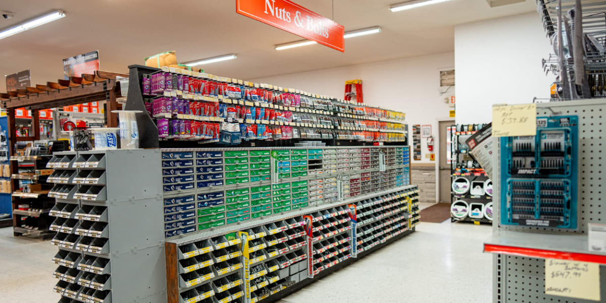 This image shows the nuts, bolts, and fasteners aisle in a hardware store, with extensive shelving systems displaying hundred
