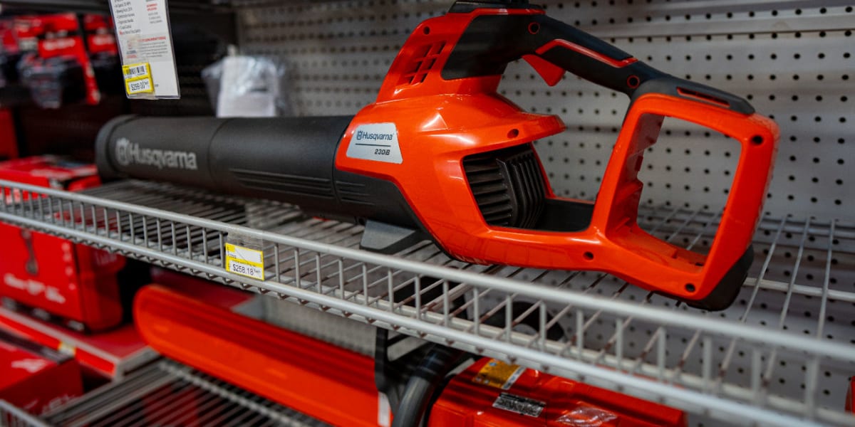A Husqvarna cordless leaf blower displayed on a wire shelf in a retail store setting