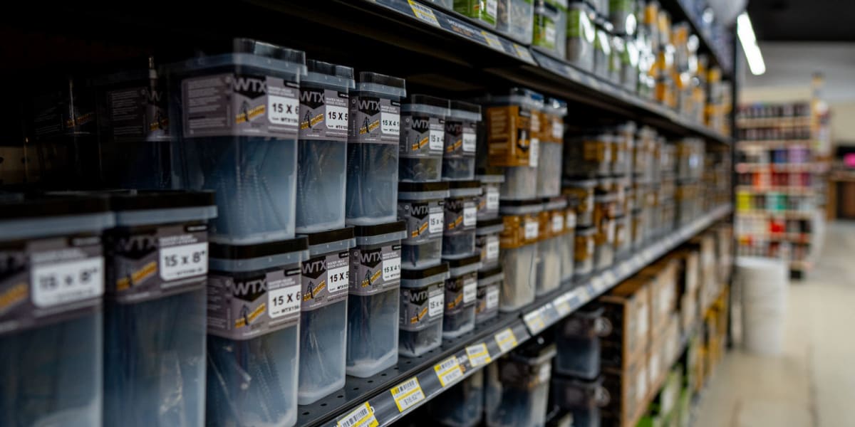 Interior view of a hardware store aisle showing shelves stocked with various boxed products and hardware items