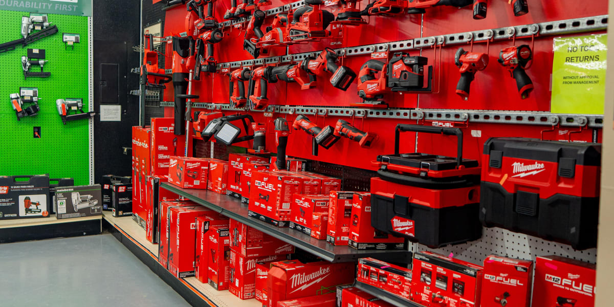 This image shows a comprehensive Milwaukee tool display in the tools department, featuring a bright red wall-mounted display