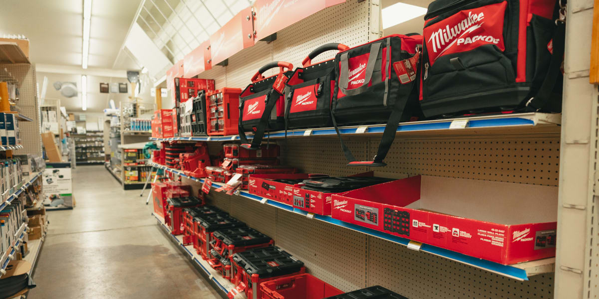 Interior view of a hardware store's tool aisle showing multiple shelves of Milwaukee tool storage products including red and
