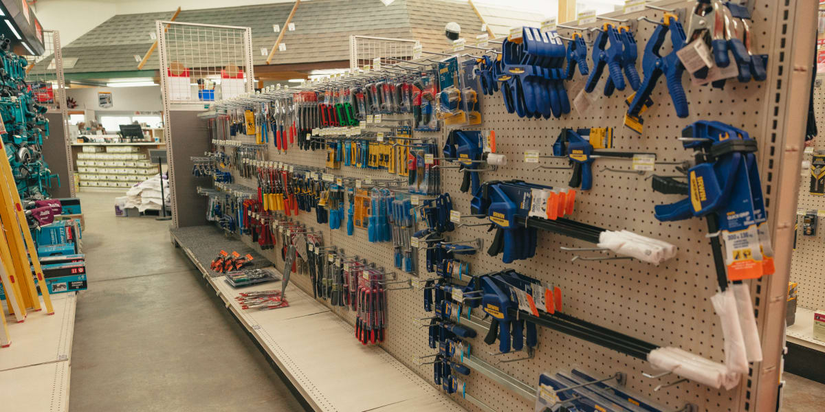 Interior view of a hardware store's tool aisle showing extensive pegboard displays with blue-handled tools and clamps organiz