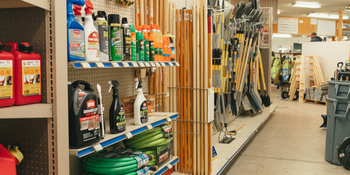 Interior view of a hardware store aisle showing shelving units with various automotive and maintenance supplies including gar