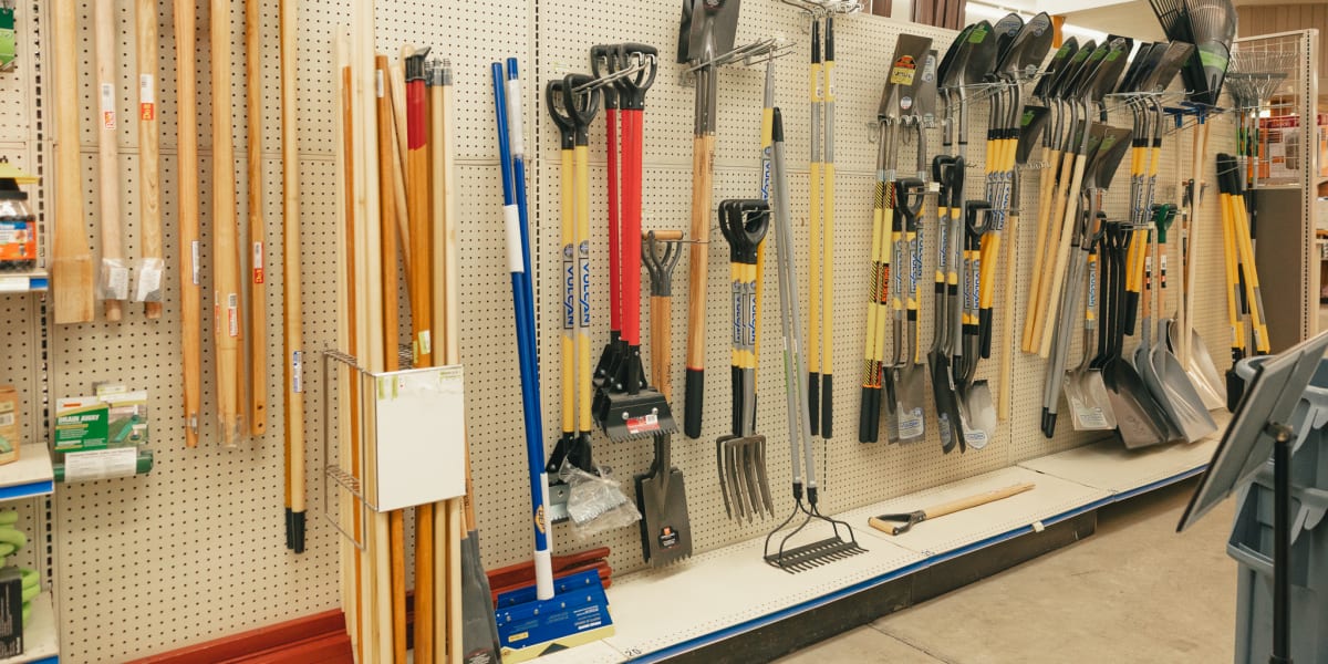 Interior view of a hardware store's tool section showing an extensive wall display of garden and yard tools