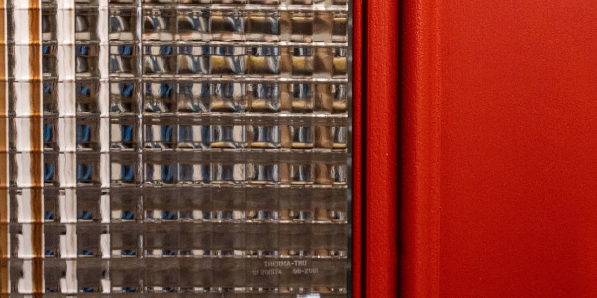 Close-up detail shot of a red-framed window showing textured or patterned glass with a grid pattern