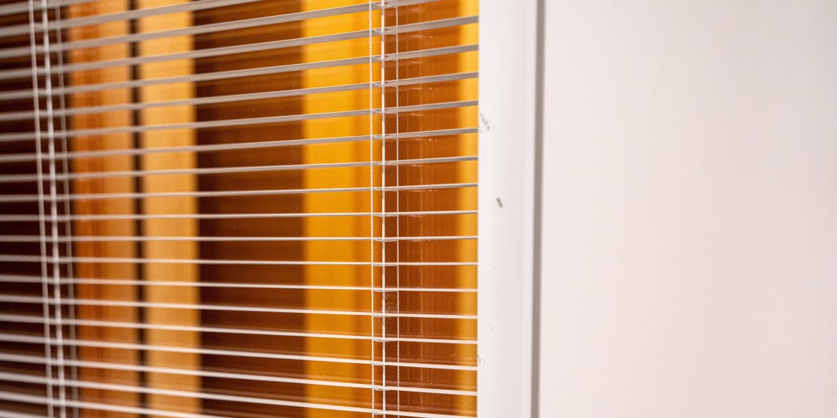 Close-up view of horizontal window blinds with white slats and control cords, mounted in a white window frame