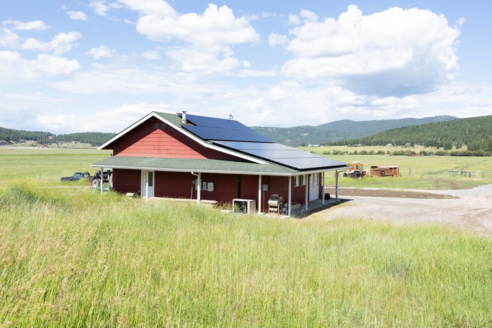 Red Montana barn with a rooftop solar array, standing in an open grass field below distant mountains