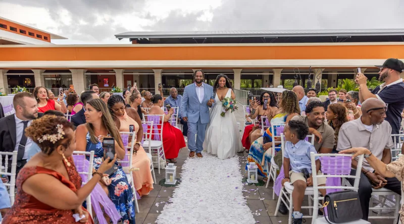 Bride and groom walk down the aisle at a Santo Domingo beach wedding under an orange canopy, surrounded by celebrating family
