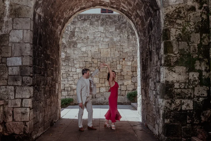 Couple beneath stone arch of colonial ruins in Santo Domingo during marriage proposal session with filtered natural light