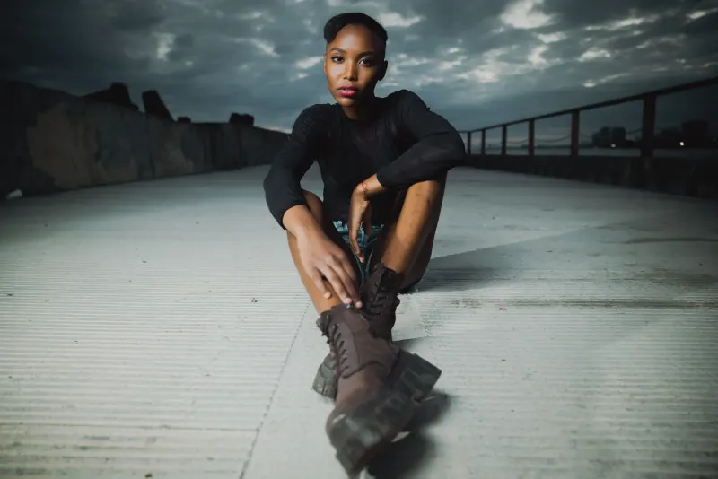 Professional urban portrait in Santo Domingo: woman in black overcoat on rooftop with dramatic cloudy sky and metal railing