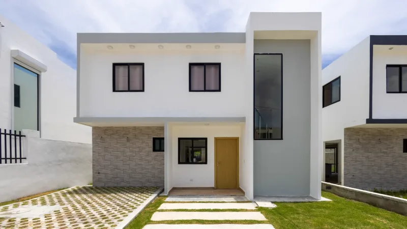 Two-story modern residence with white facade, brick details, and pedestrian entry in Santo Domingo. Real estate photography with midday natural light.