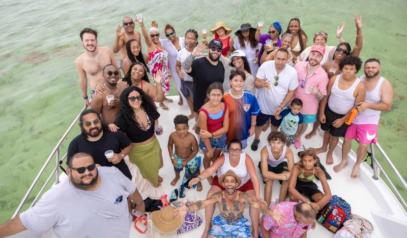Large family group on Punta Cana boat smiling at camera, turquoise water background, golden natural light illuminating faces