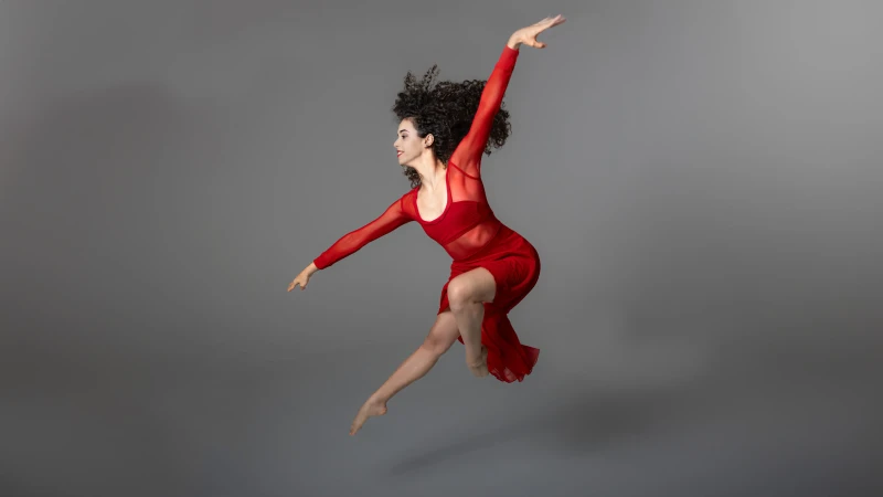 Dancer in flight wearing red costume against neutral grey background; artistic movement photography in Santo Domingo studio