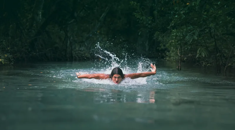Family river session: child swimming in crystalline waters with open arms among tropical vegetation in Santo Domingo