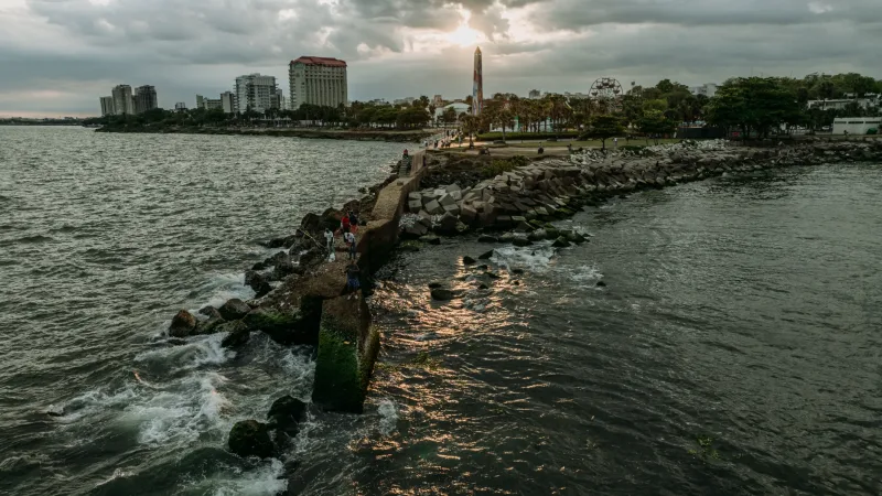 Family posing on the jetty of Santo Domingo's Malecón with coastal architecture and cloudy sky in background, professional family photography session