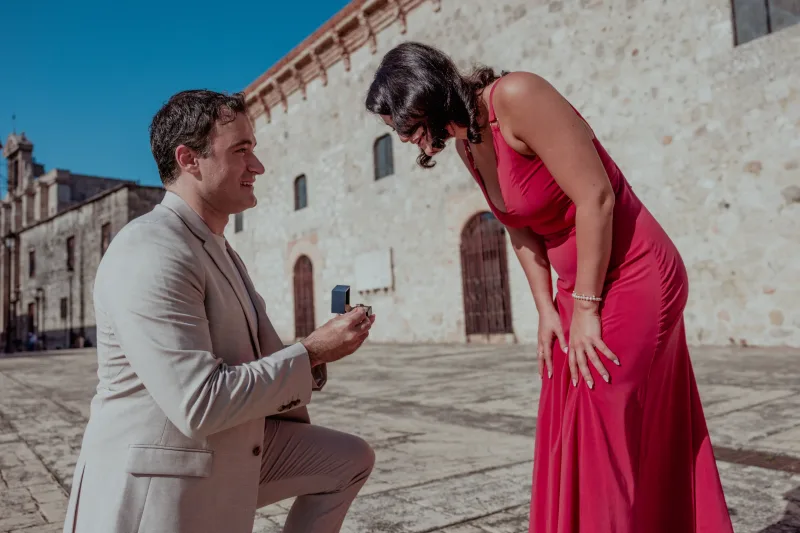 Man in beige suit proposes with diamond ring to woman in fuchsia dress in Santo Domingo's colonial plaza