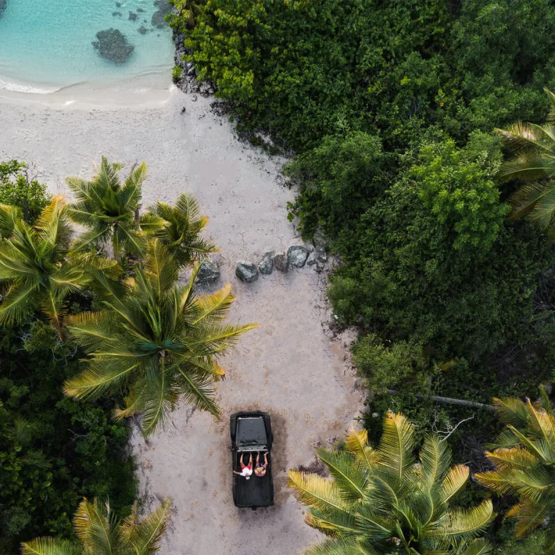 Black car parked on white Caribbean beach sand with smiling family, surrounded by mangroves and turquoise water during family photography session