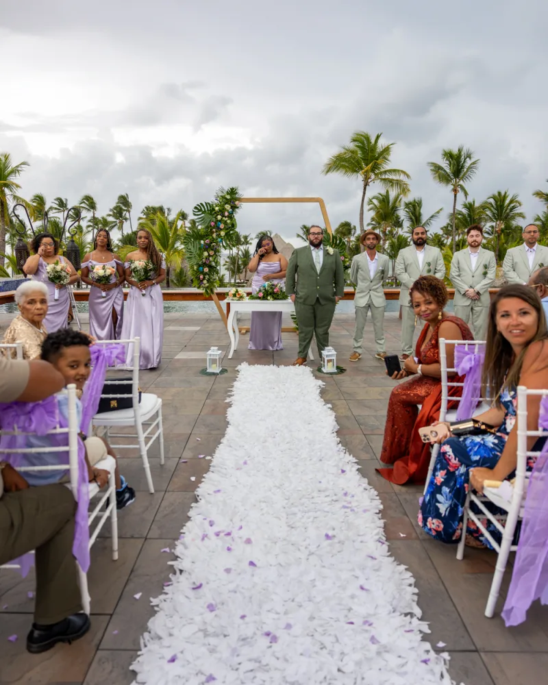 Tropical wedding ceremony in Punta Cana with wooden arch, couple exchanging vows, palm trees in background, purple petals on white sand