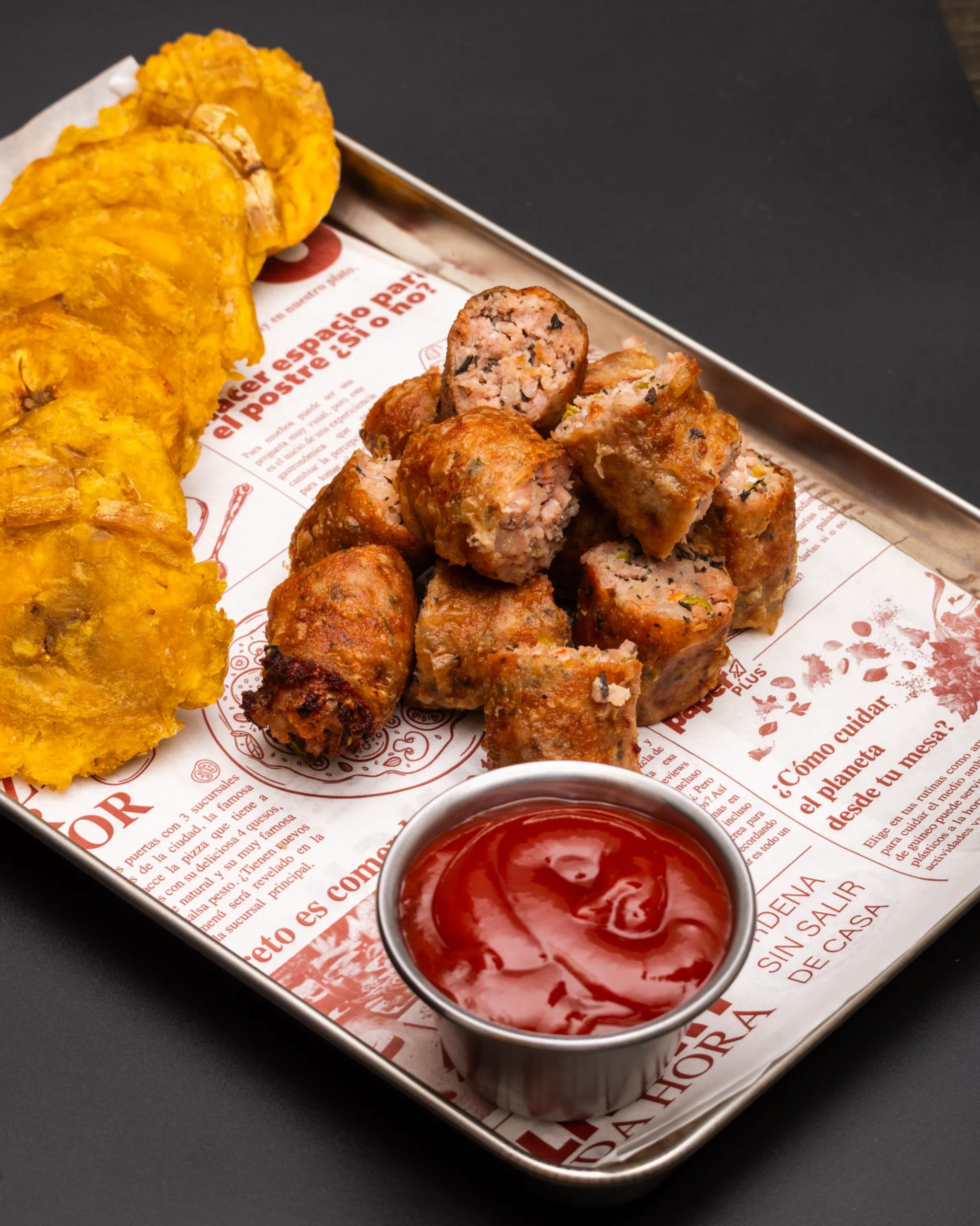 Fried croquetas with tostones and ketchup dip on a branded metal tray