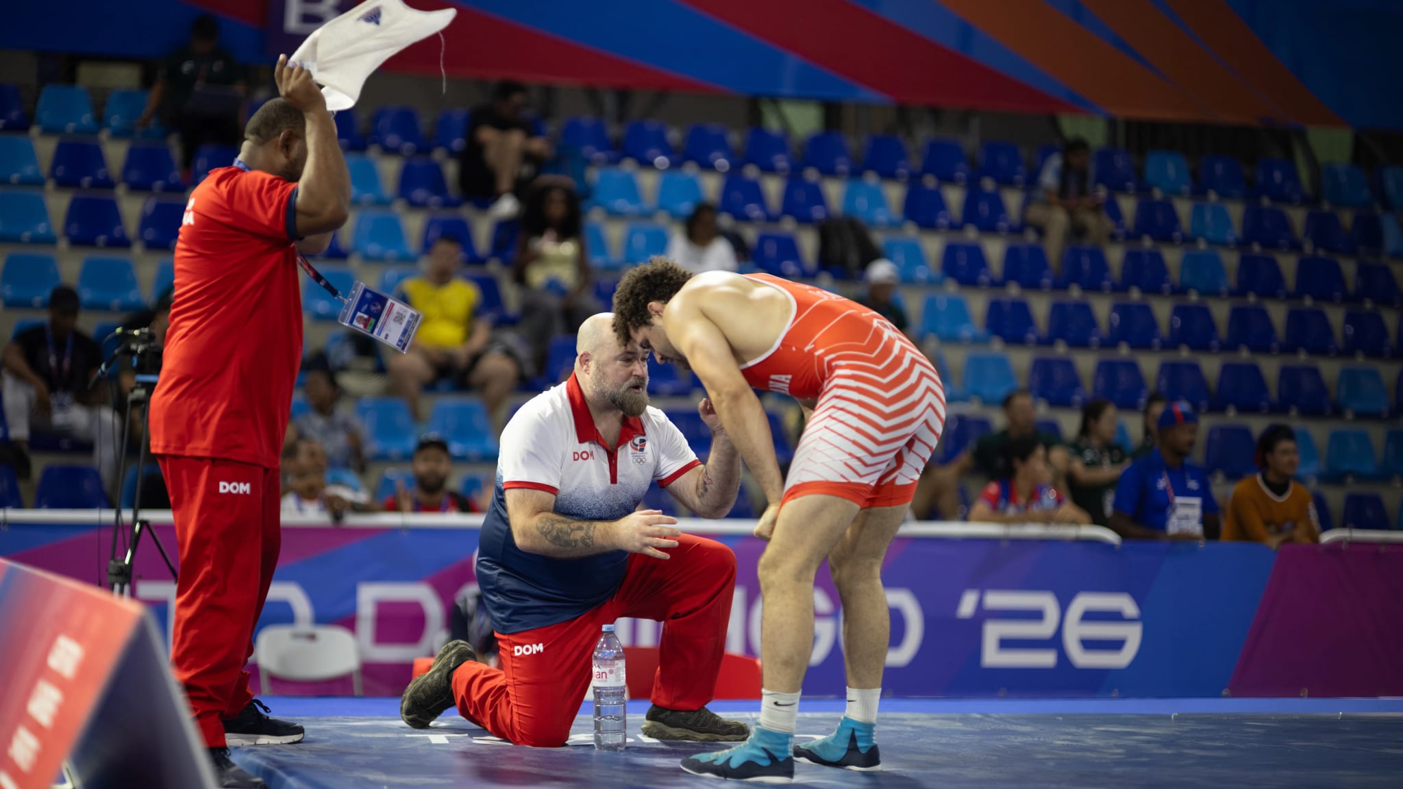 Coach attending to an Olympic wrestling athlete between rounds, with stands in the background