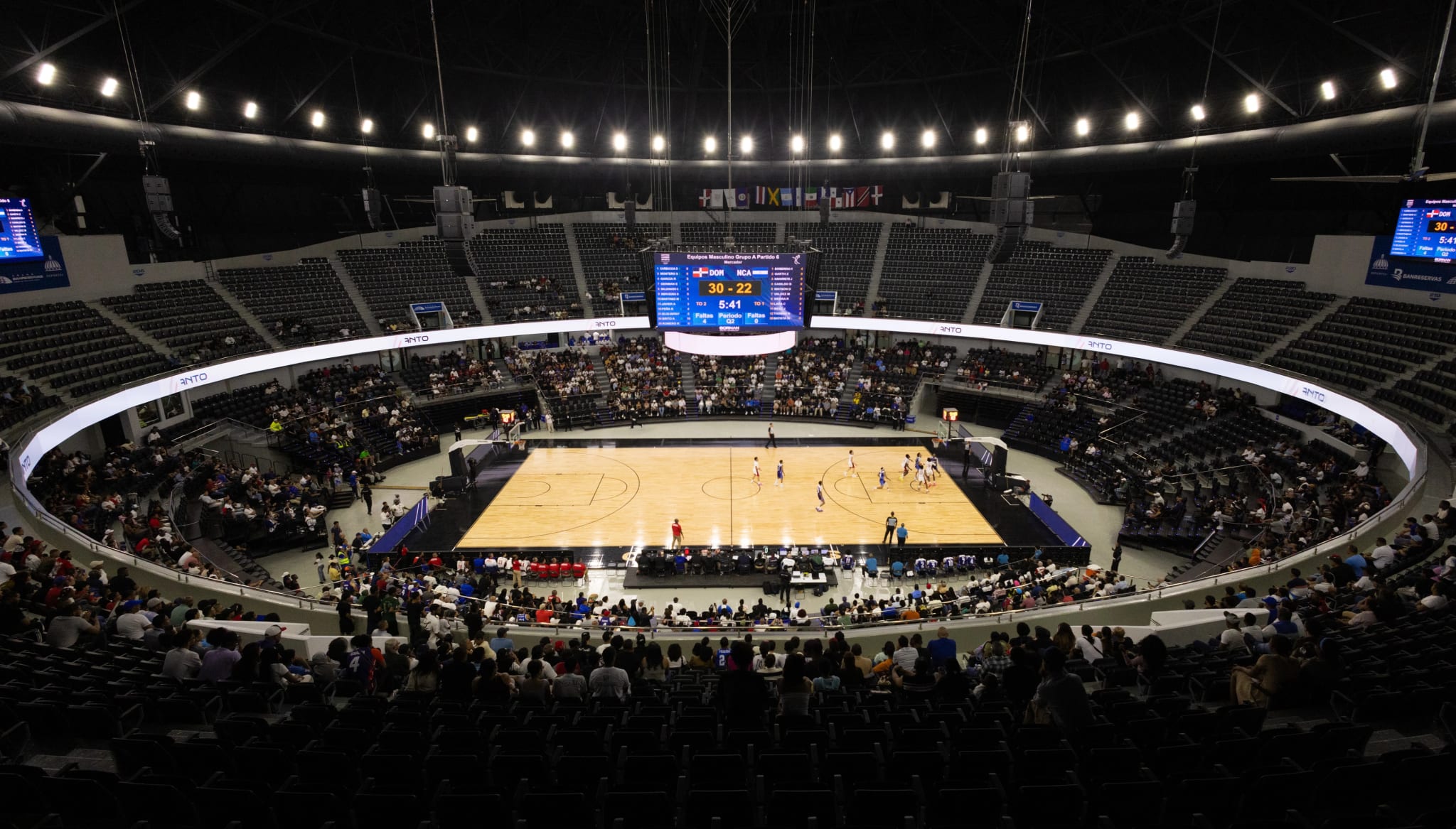 Elevated wide view of a full basketball arena during a game, with scoreboard and crowd