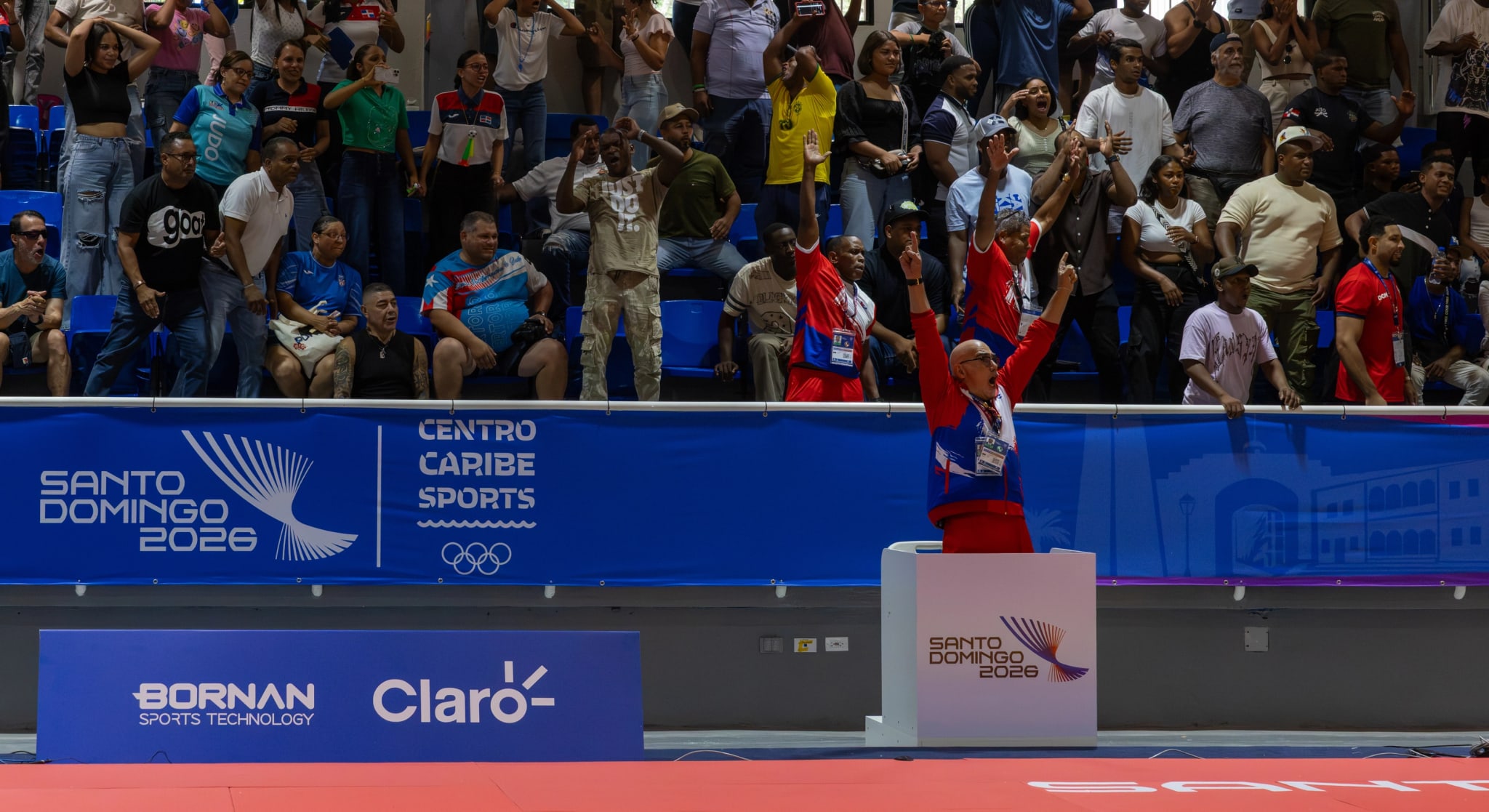 Athlete celebrating on the podium during a medal ceremony, with the crowd standing