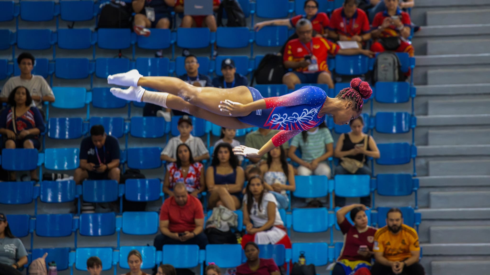 Gymnast mid-air during an artistic gymnastics routine, with crowd in the stands