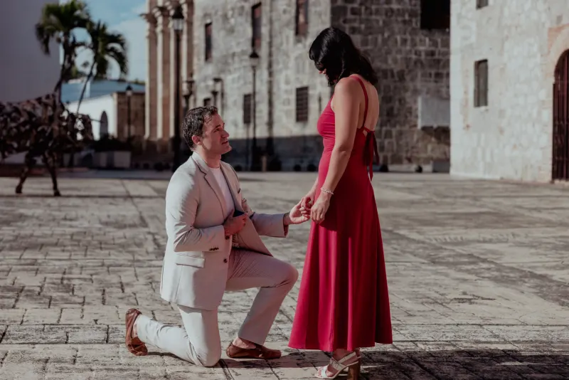 Man in white suit kneeling before woman in red dress in Santo Domingo colonial plaza proposal photography moment