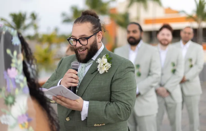 Groom in mint-green suit and glasses delivers speech at Santo Domingo wedding ceremony, surrounded by groomsmen