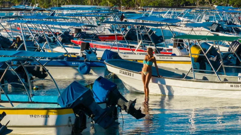 Woman in turquoise water surrounded by traditional blue fishing boats during beach photo session in Samaná, Dominican Republic