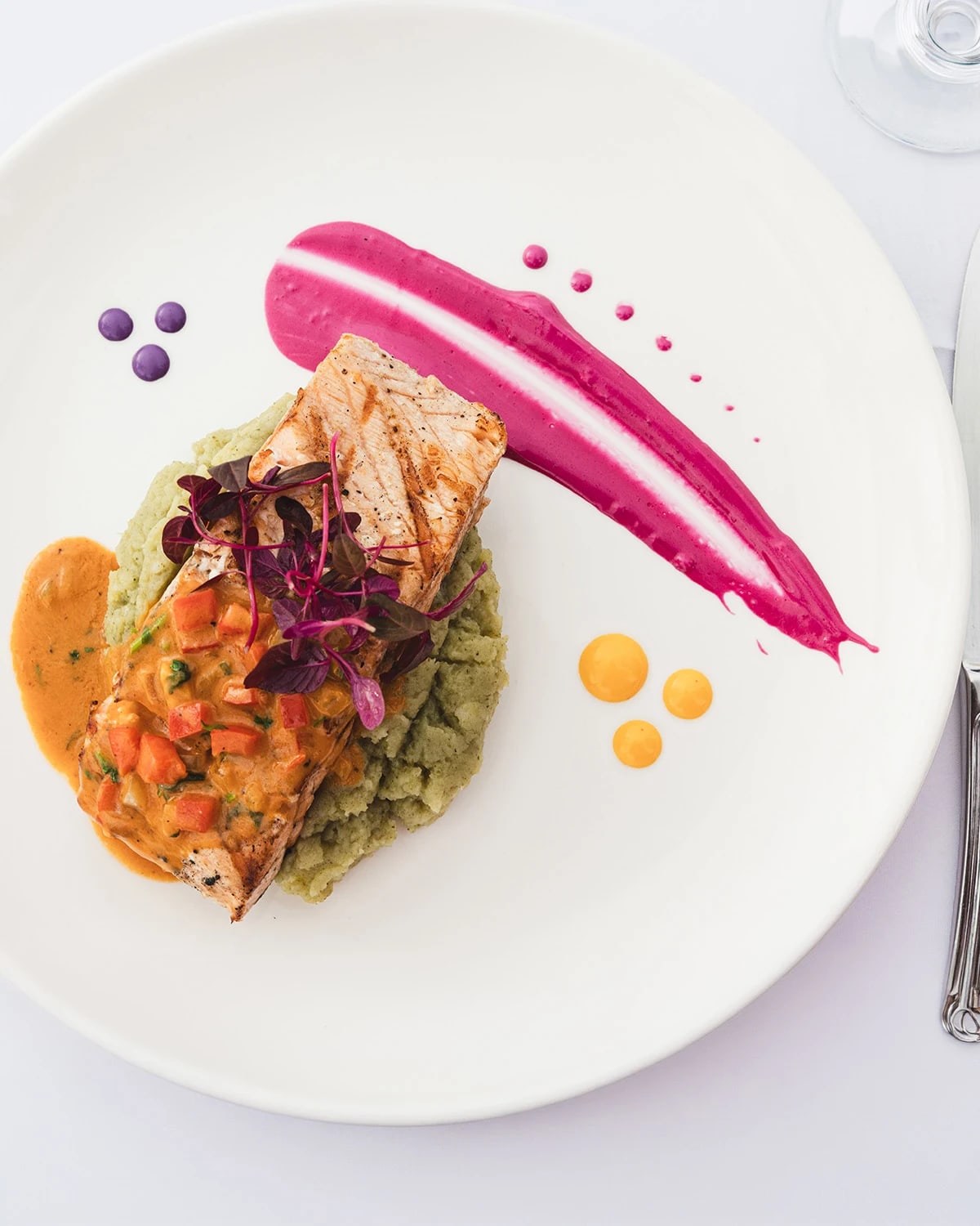Filete de pescado sellado sobre puré de aguacate con hierbas y salsa de frutas vibrante, montaje de alta cocina