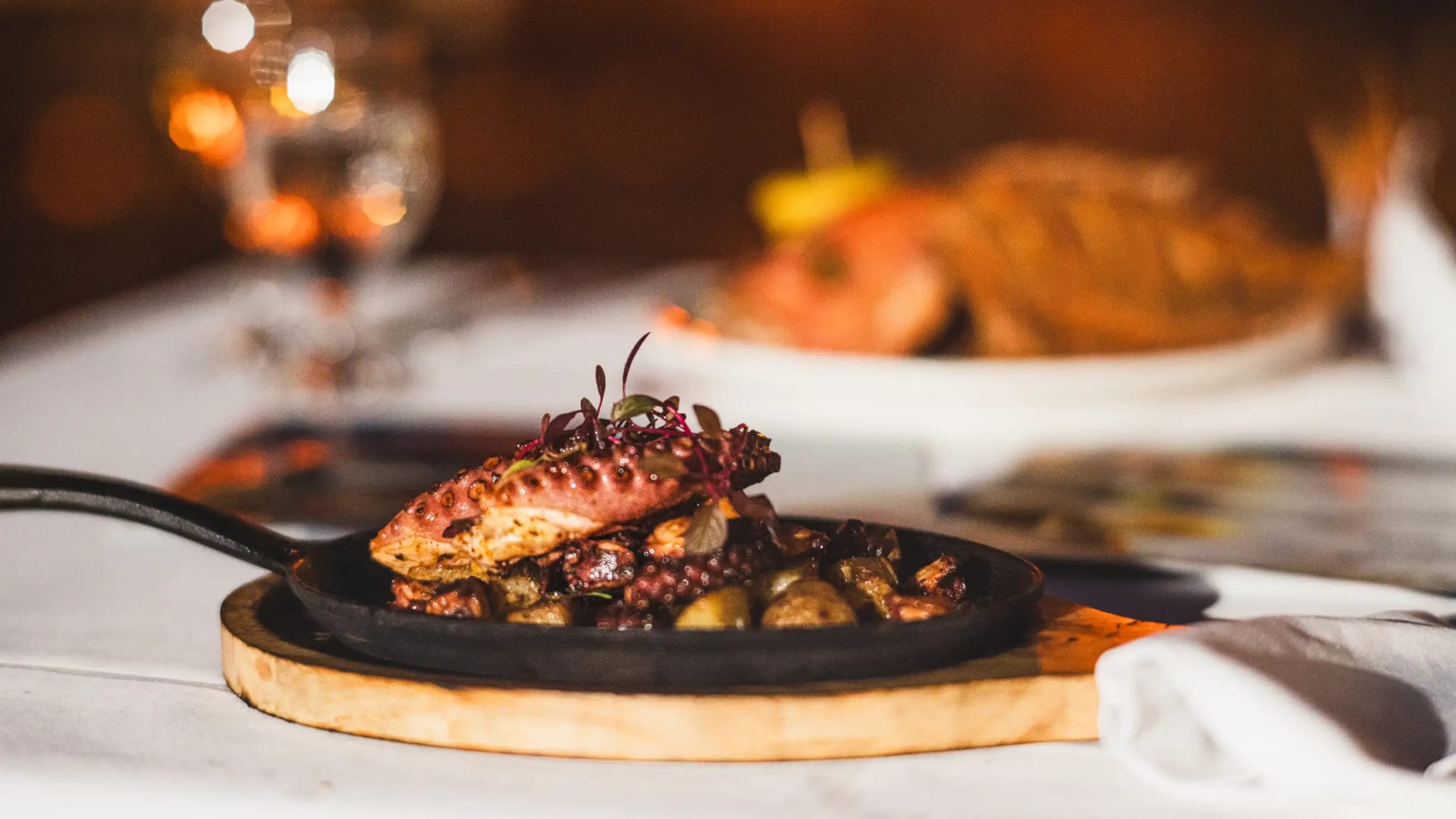 Pulpo a la parrilla servido en sartén de hierro fundido con aceitunas, ambiente cálido del restaurante