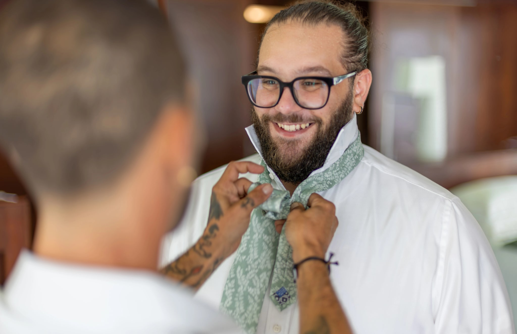 Novio sonriendo mientras su padrino le ajusta una bufanda estampada
