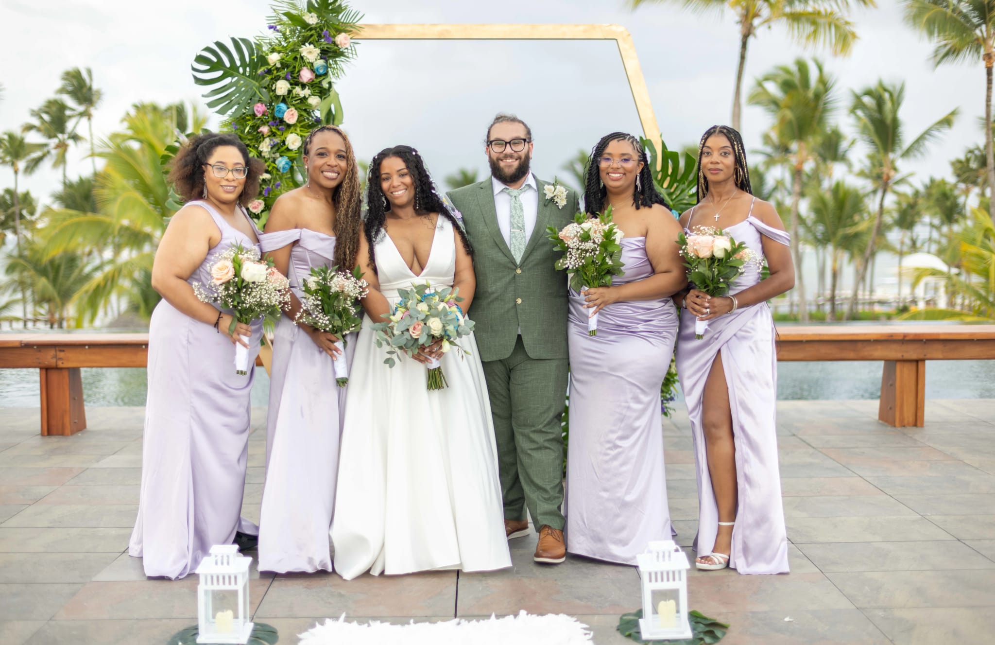 Novios junto al cortejo nupcial bajo un arco floral tropical