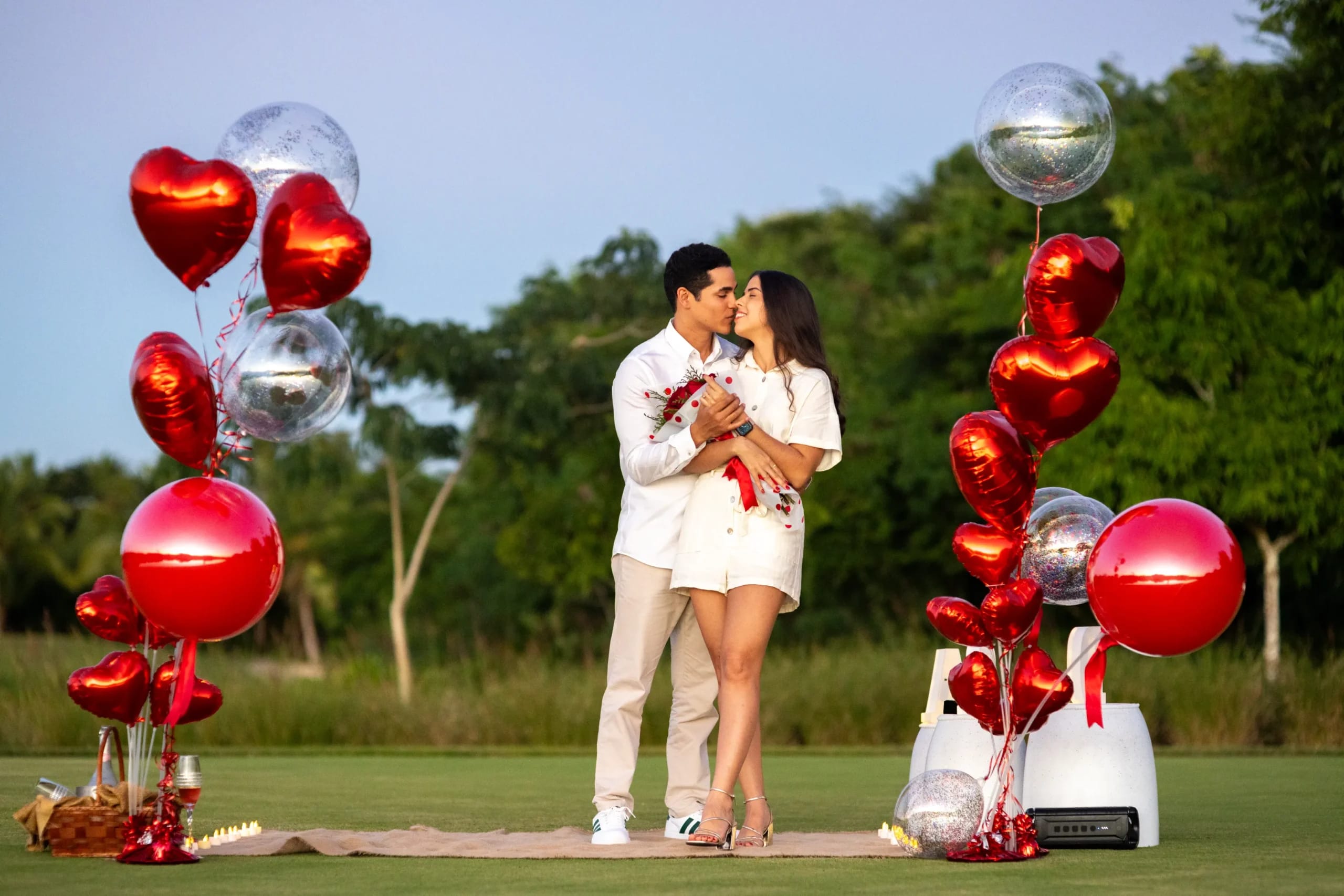Pareja besándose en la playa junto a globos de corazón rojos en Punta Cana