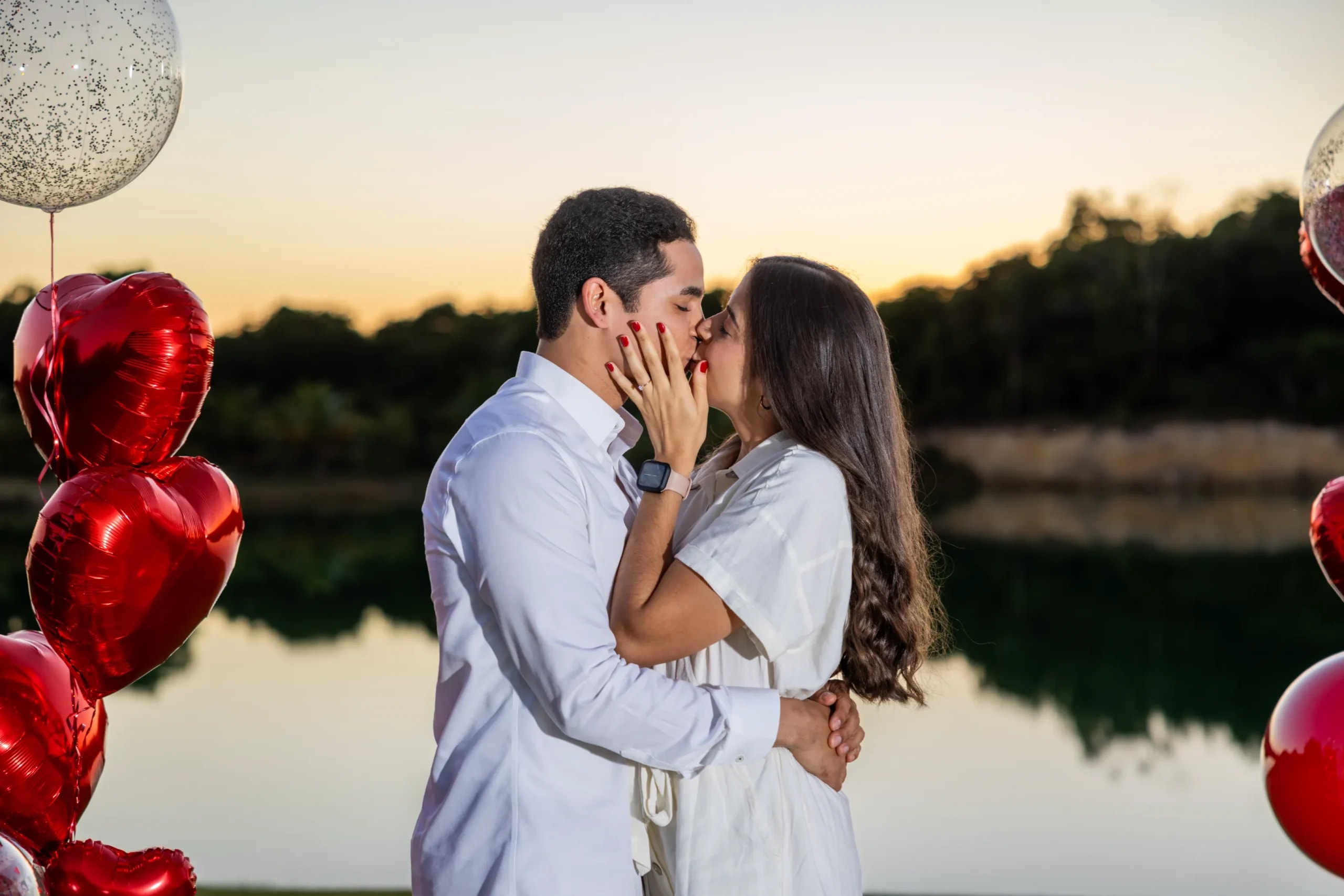 Pareja besándose después de la propuesta de matrimonio junto al lago al atardecer