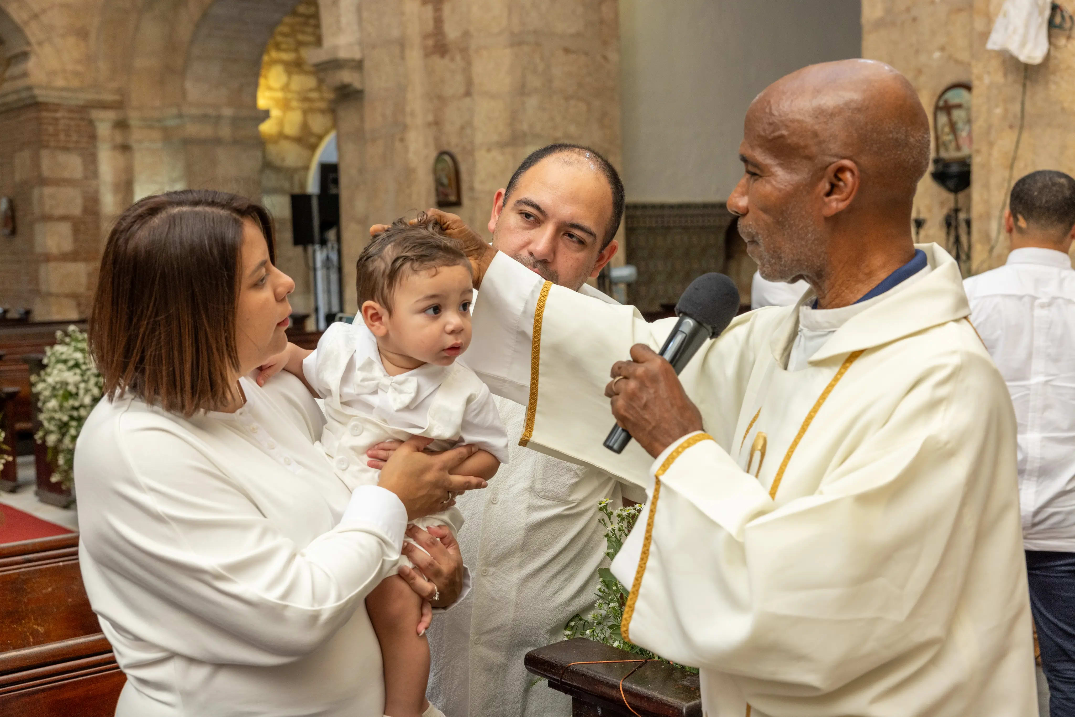 Sacerdote bendiciendo a una bebé en brazos de sus padres dentro de una iglesia colonial de piedra, Santo Domingo — Babula Shots